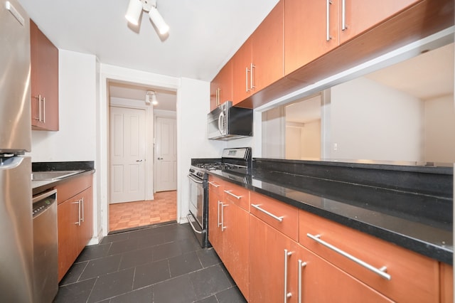 300 W 135th St Unit 4L, New York City, NY 10030 - kitchen with appliances with stainless steel finishes, brown cabinetry, dark stone counters, and dark tile patterned flooring