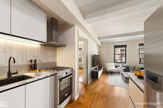 102 E 22nd St Unit 3B, New York City, NY 10010 - kitchen with wall chimney range hood, white gas stove, light wood-style floors, light countertops, and tasteful backsplash