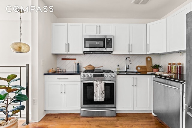 120 Pulaski St Unit 1B, New York City, NY 11206 - kitchen featuring appliances with stainless steel finishes, dark countertops, light wood-type flooring, decorative backsplash, and white cabinetry