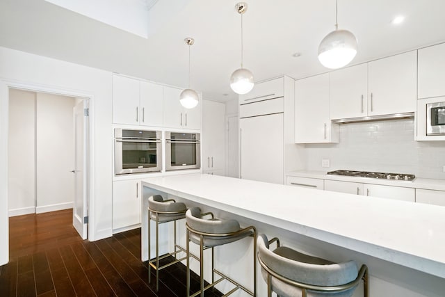 229 E 79th St Unit 7-B, New York City, NY 10075 - kitchen featuring a breakfast bar area, stainless steel appliances, light countertops, dark wood-type flooring, and tasteful backsplash