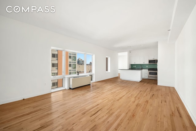 304 W 115th St Unit 6A, New York City, NY 10026 - unfurnished living room with radiator heating unit and light wood-style flooring
