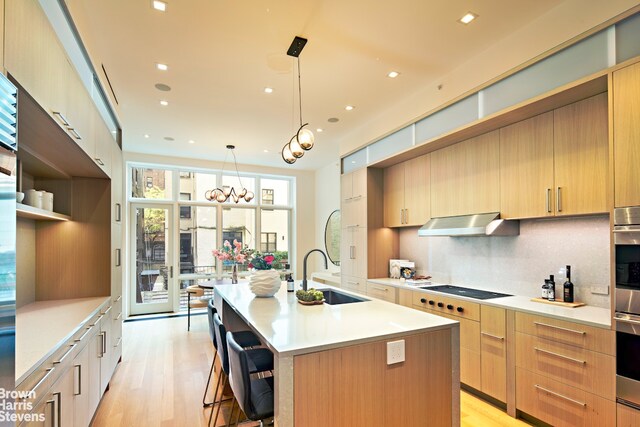 6 W 95th St, New York City, NY 10025 - kitchen featuring modern cabinets, light countertops, a kitchen island with sink, decorative backsplash, and light wood finished floors