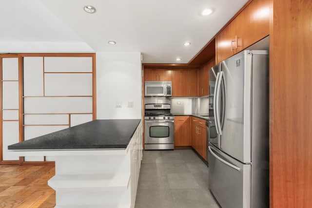 16 W 16th St Unit 7Rn, New York City, NY 10011 - kitchen with appliances with stainless steel finishes, a peninsula, dark countertops, brown cabinetry, and recessed lighting