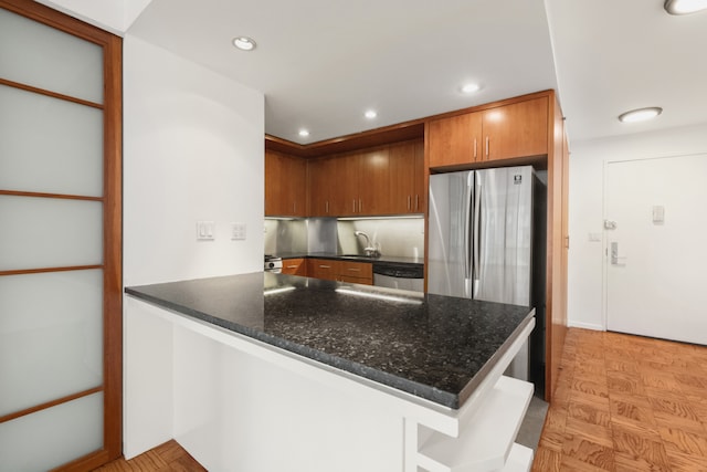 16 W 16th St Unit 7Rn, New York City, NY 10011 - kitchen featuring a peninsula, stainless steel appliances, dark stone countertops, brown cabinetry, and recessed lighting