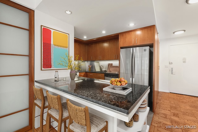 16 W 16th St Unit 7Rn, New York City, NY 10011 - kitchen with appliances with stainless steel finishes, brown cabinetry, dark stone countertops, a breakfast bar area, and a peninsula
