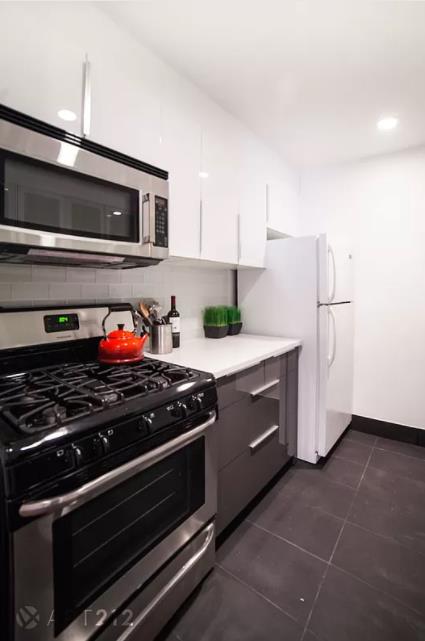 179 Grand St Unit 2-F, New York City, NY 10013 - kitchen featuring stainless steel appliances, white cabinetry, backsplash, dark tile patterned flooring, and light countertops