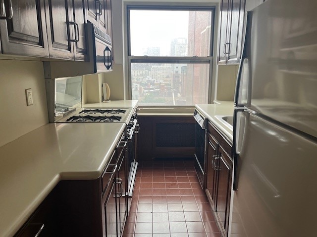 215 E 79th St Unit 12B, New York City, NY 10075 - kitchen featuring freestanding refrigerator, light countertops, white range with gas stovetop, wainscoting, and dark tile patterned floors