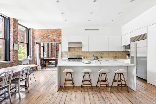 525 W 22nd St Unit 3Af, New York City, NY 10011 - kitchen featuring built in appliances, range hood, light countertops, white cabinets, and brick wall