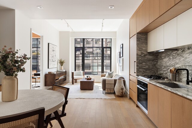 517 W 29th St Unit 8B, New York City, NY 10001 - kitchen with oven, light wood finished floors, decorative backsplash, stainless steel gas cooktop, and light stone counters