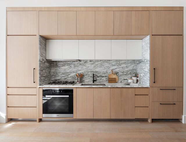 517 W 29th St Unit 8B, New York City, NY 10001 - kitchen featuring wall oven, backsplash, light stone countertops, light brown cabinetry, and light wood finished floors
