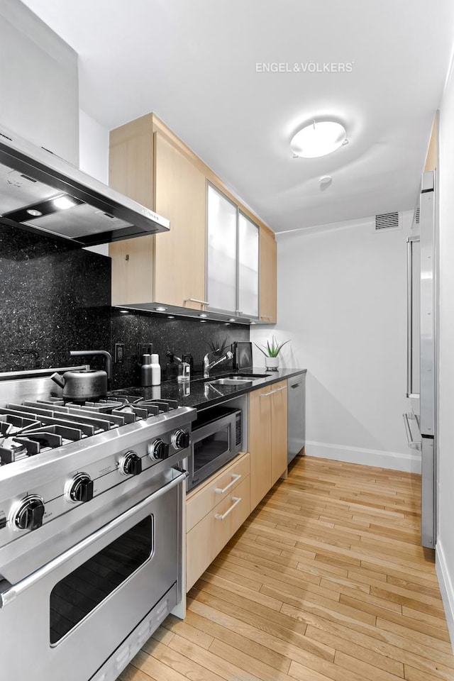 121 W 19th St Unit 3D, New York City, NY 10011 - kitchen with stainless steel appliances, wall chimney range hood, light brown cabinets, and decorative backsplash