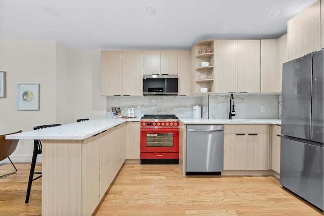 449 Pulaski St, New York City, NY 11221 - kitchen featuring stainless steel appliances, a peninsula, light wood-type flooring, light brown cabinets, and tasteful backsplash