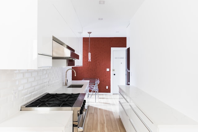 32 Jones St Unit 2D, New York City, NY 10014 - kitchen featuring gas range, wall chimney range hood, white cabinetry, light wood-style floors, and decorative backsplash