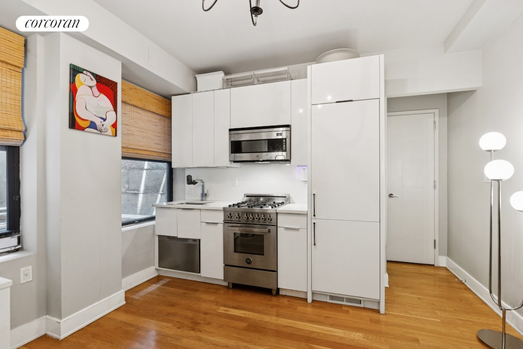 308 W 30th St Unit 1A, New York City, NY 10001 - kitchen featuring appliances with stainless steel finishes, white cabinets, light countertops, light wood-style flooring, and modern cabinets