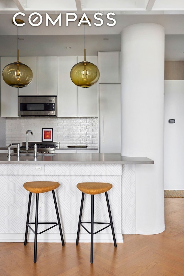 184 Kent Ave Unit B503, New York City, NY 11249 - kitchen featuring stainless steel microwave, a breakfast bar area, tasteful backsplash, hanging light fixtures, and white cabinets