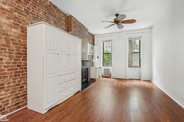 433 W 46th St Unit 1Rw, New York City, NY 10036 - unfurnished living room featuring radiator heating unit, wood finished floors, brick wall, ceiling fan, and a glass covered fireplace