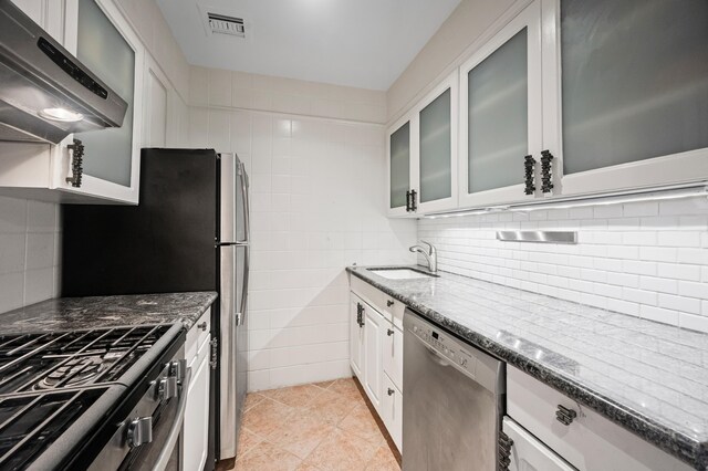 250 W 15th St Unit 6F, New York City, NY 10011 - kitchen featuring appliances with stainless steel finishes, wall chimney range hood, dark stone counters, white cabinetry, and tasteful backsplash