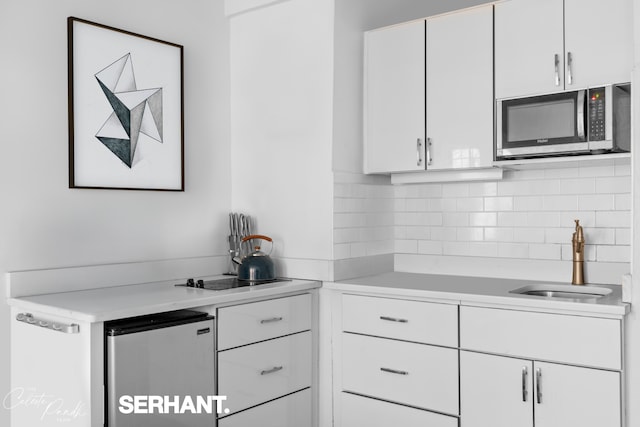 320 E 42nd St Unit 705, New York City, NY 10017 - kitchen featuring stainless steel microwave, light countertops, white cabinets, fridge, and decorative backsplash