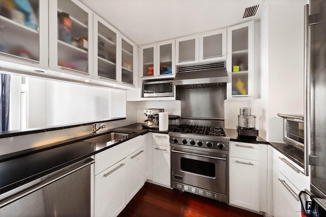 45 Park Ave Unit 1105, New York City, NY 10016 - kitchen with stainless steel appliances, under cabinet range hood, dark countertops, white cabinetry, and dark wood-style flooring