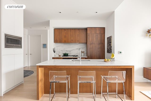 509 Pacific St Unit 4J, New York City, NY 11217 - kitchen featuring stainless steel microwave, modern cabinets, brown cabinets, a kitchen bar, and decorative backsplash