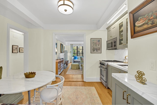 235 E 22nd St Unit 5C, New York City, NY 10010 - kitchen with appliances with stainless steel finishes, gray cabinetry, light wood-style flooring, and glass insert cabinets
