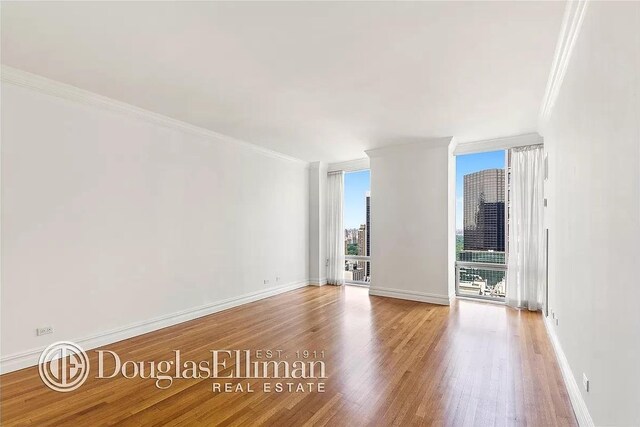 641 5th Ave Unit 35D, New York City, NY 10022 - spare room featuring ornamental molding, healthy amount of natural light, wood finished floors, a wall of windows, and a view of city