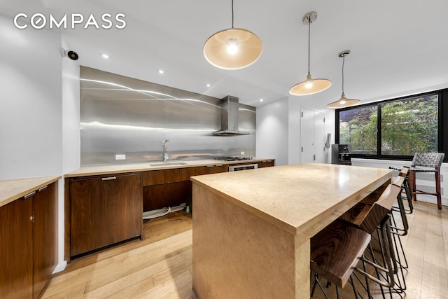 515 E 72nd St Unit 36B, New York City, NY 10021 - kitchen featuring wall chimney range hood, light countertops, light wood-style flooring, a center island, and hanging light fixtures