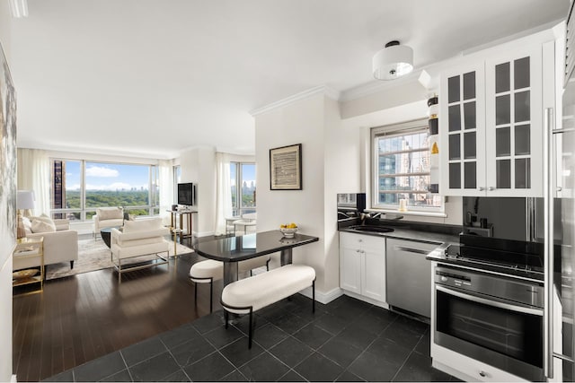 301 W 57th St Unit 16C, New York City, NY 10019 - kitchen with stainless steel appliances, dark countertops, crown molding, white cabinets, and healthy amount of natural light