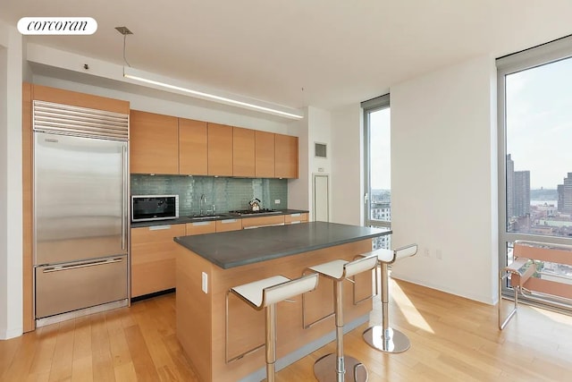 310 W 52nd St Unit 18H, New York City, NY 10019 - kitchen featuring stainless steel built in refrigerator, light wood finished floors, dark countertops, and decorative backsplash