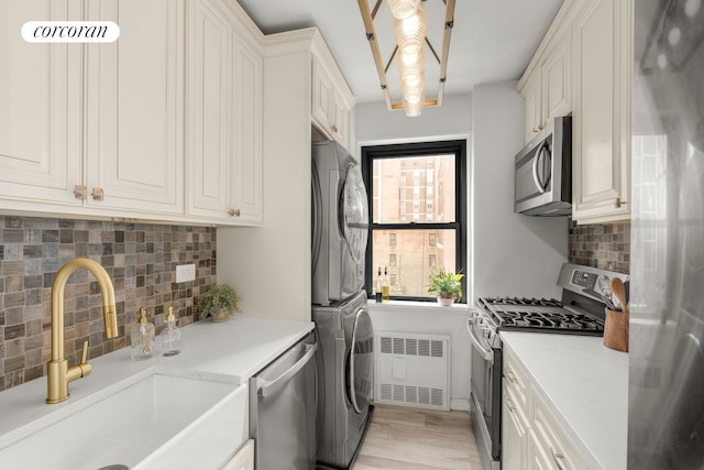 136 E 76th St Unit 10C, New York City, NY 10021 - kitchen featuring appliances with stainless steel finishes, radiator, estacked washer and dryer, backsplash, and white cabinets