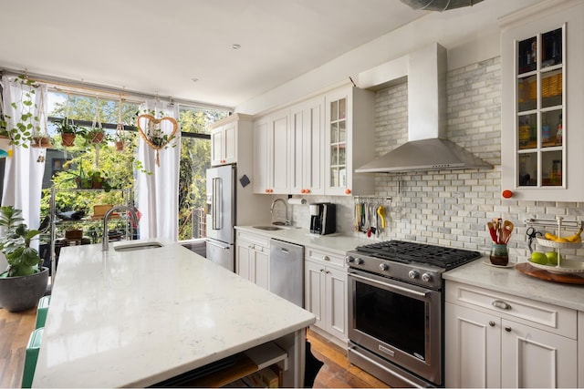 127 Cooper St, New York City, NY 11207 - kitchen with premium appliances, wall chimney exhaust hood, decorative backsplash, white cabinets, and light stone counters