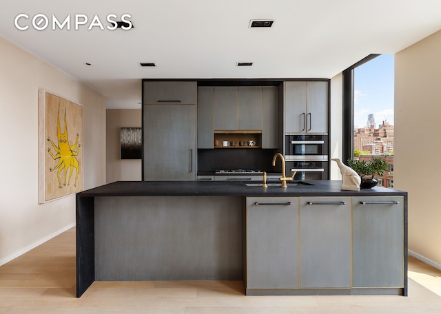505 W 19th St Unit 7B, New York City, NY 10011 - kitchen with dark countertops, modern cabinets, light wood-type flooring, a center island with sink, and gray cabinets