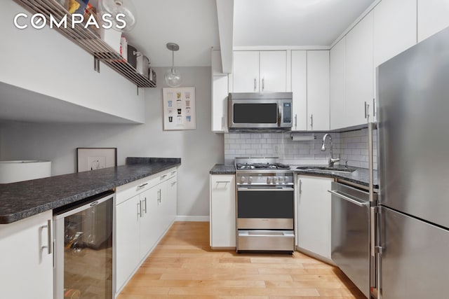 211 Thompson St Unit Gld, New York City, NY 10012 - kitchen with stainless steel appliances, beverage cooler, light wood-style flooring, white cabinets, and decorative backsplash