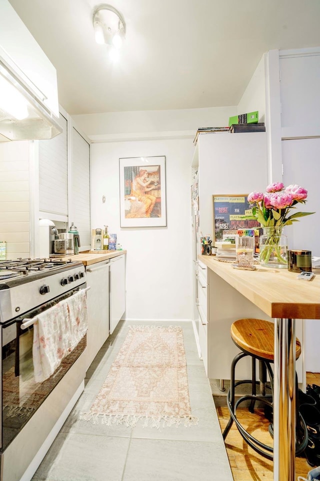 223 E 78th St Unit 2B, New York City, NY 10075 - kitchen with gas range, extractor fan, wooden counters, light tile patterned flooring, and white cabinetry