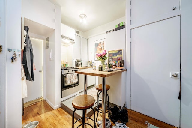223 E 78th St Unit 2B, New York City, NY 10075 - kitchen with stainless steel range with gas stovetop, light wood-style floors, white cabinetry, under cabinet range hood, and wooden counters