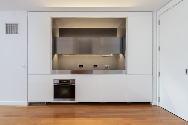 15 William St Unit 39F, New York City, NY 10004 - kitchen with stainless steel oven, light wood-style floors, and white cabinetry
