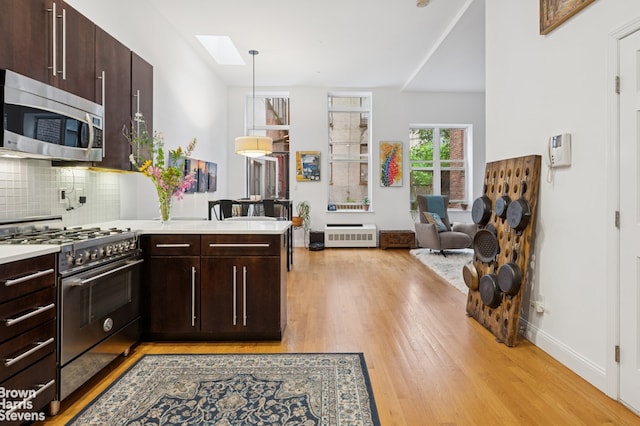 302 W 122nd St Unit 1, New York City, NY 10027 - kitchen with stainless steel appliances, a peninsula, light wood-style floors, dark brown cabinets, and decorative backsplash