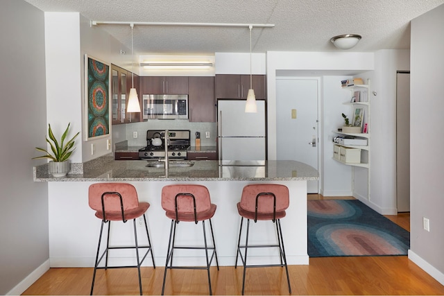 555 W 23rd St Unit N7H, New York City, NY 10011 - kitchen with appliances with stainless steel finishes, a peninsula, a breakfast bar area, light wood-type flooring, and a textured ceiling