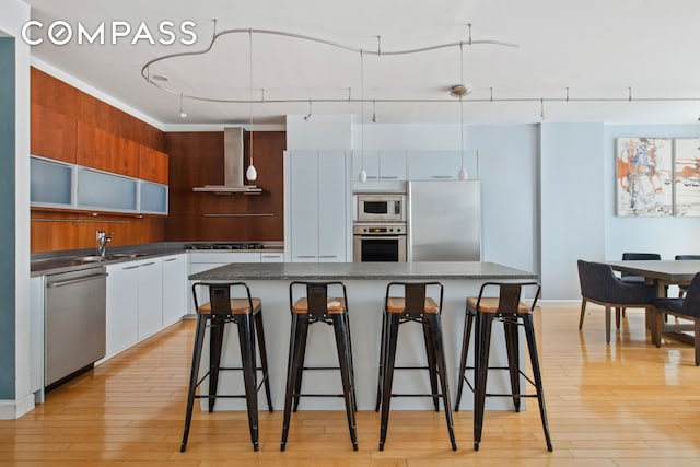 151 W 17th St Unit 5A, New York City, NY 10011 - kitchen featuring wall chimney exhaust hood, stainless steel appliances, modern cabinets, a kitchen bar, and a center island