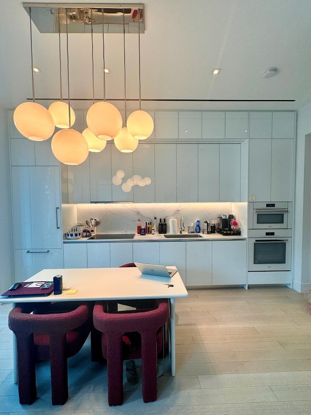 200 E 59th St Unit 8B, New York City, NY 10022 - kitchen featuring modern cabinets, double oven, light wood finished floors, white cabinetry, and decorative light fixtures