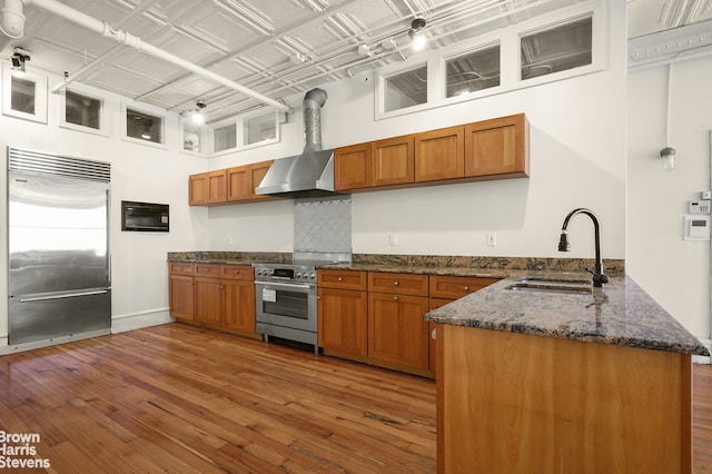 547 Broadway Unit 3, New York City, NY 10012 - kitchen featuring premium appliances, a peninsula, brown cabinets, wall chimney range hood, and a towering ceiling