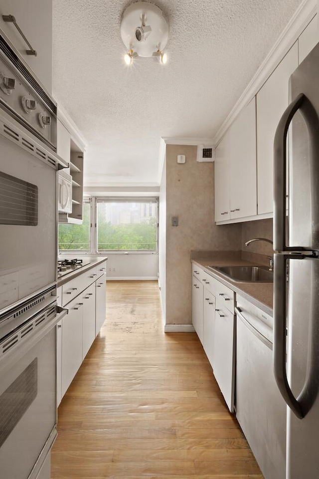 180 Park Row Unit 5B, New York City, NY 10038 - kitchen with appliances with stainless steel finishes, ornamental molding, a textured ceiling, white cabinetry, and light wood-style floors
