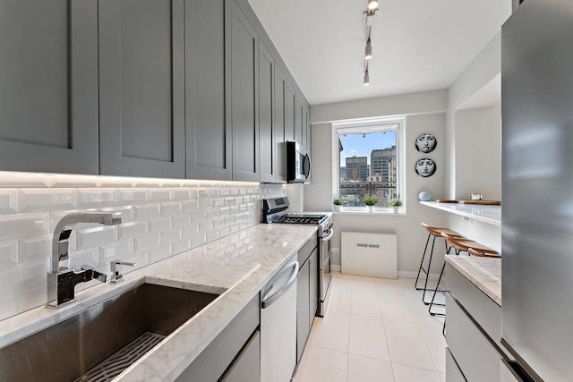 20 E 68th St Unit 12D, New York City, NY 10065 - kitchen featuring stainless steel appliances, gray cabinetry, decorative backsplash, and light stone counters