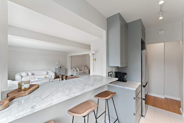 20 E 68th St Unit 12D, New York City, NY 10065 - kitchen featuring gray cabinets, light stone countertops, a breakfast bar, open floor plan, and a decorative wall