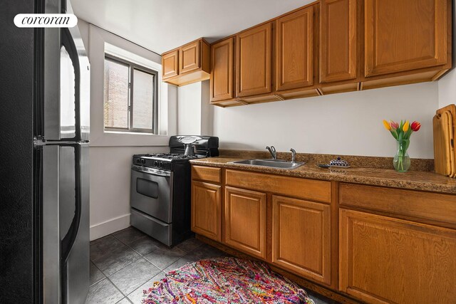 66 Putnam Ave, New York City, NY 11238 - kitchen with stainless steel gas range oven, freestanding refrigerator, brown cabinetry, dark countertops, and tile patterned flooring