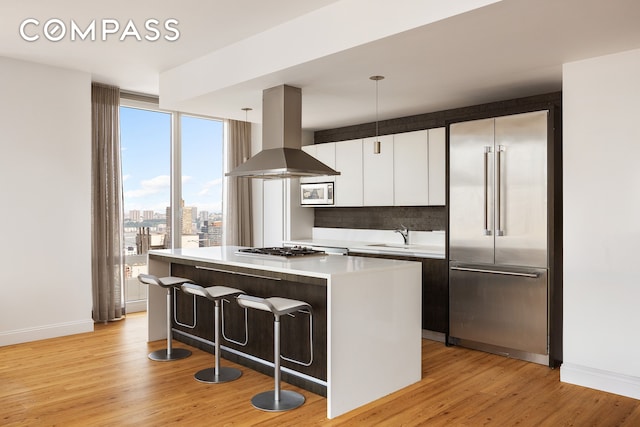 247 W 46th St Unit 3103, New York City, NY 10036 - kitchen featuring built in appliances, wall chimney exhaust hood, a center island, light wood-style floors, and a kitchen breakfast bar