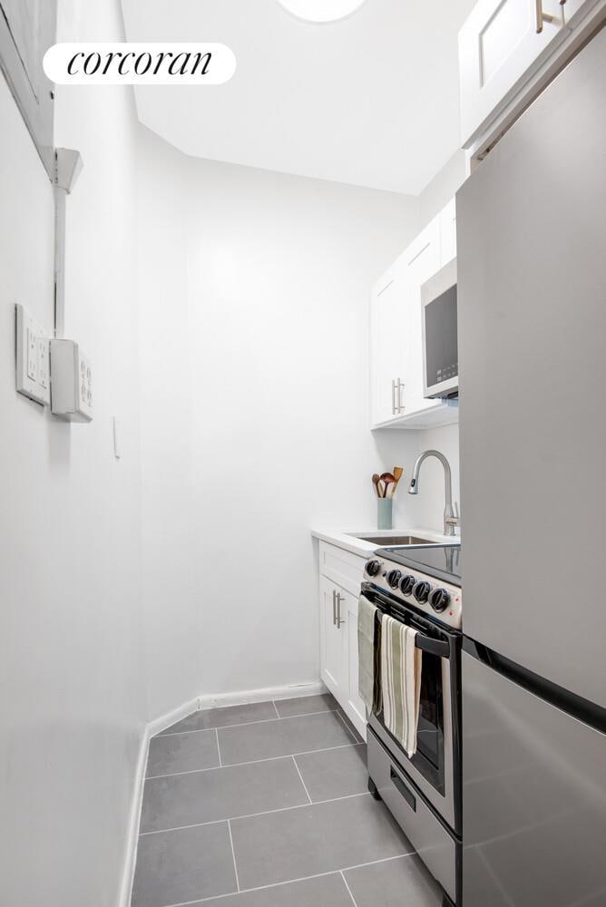 390 W End Ave Unit 1Dn, New York City, NY 10024 - kitchen featuring appliances with stainless steel finishes, white cabinetry, dark tile patterned floors, and light countertops