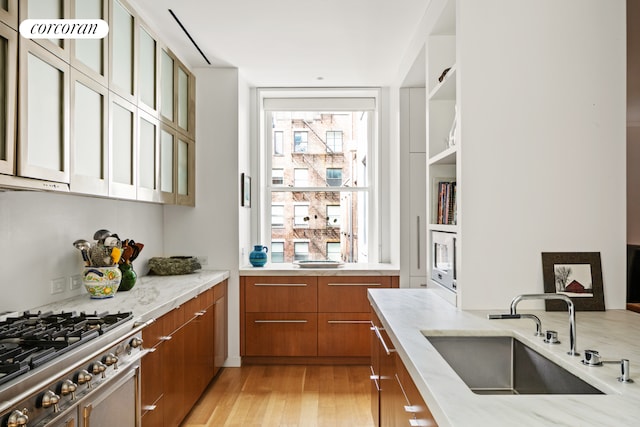 7 Harrison St Unit 4S, New York City, NY 10013 - kitchen with brown cabinets, light stone counters, light wood-style floors, glass insert cabinets, and stainless steel range oven