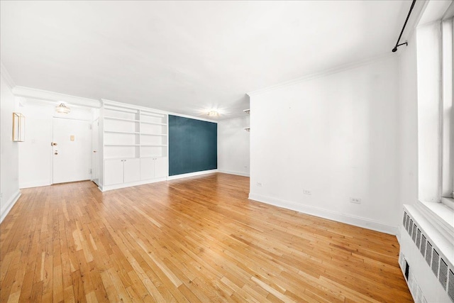 309 E 87th St Unit 7-J, New York City, NY 10128 - unfurnished living room featuring radiator heating unit, light wood-type flooring, crown molding, and built in shelves