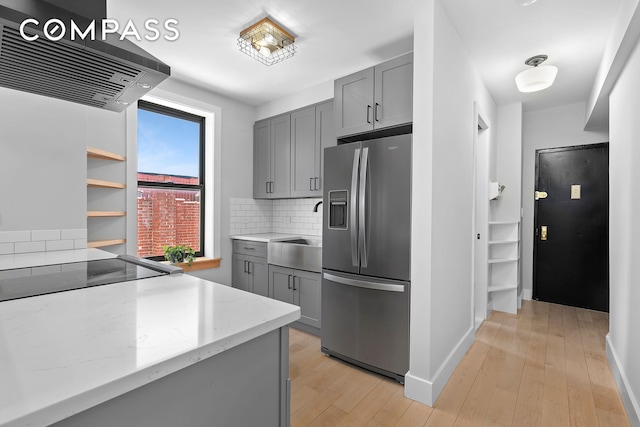 108 Division Ave Unit 22, New York City, NY 11211 - kitchen featuring stainless steel refrigerator with ice dispenser, gray cabinets, ventilation hood, backsplash, and light stone countertops